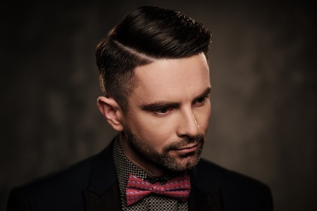 Well-groomed stylish young man with bow tie posing on dark background.の写真素材