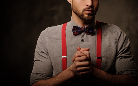 Young handsome man with beard wearing suspenders and posing on dark background.の写真素材