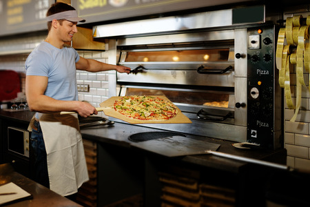 Handsome pizzaiolo making pizza at kitchen in pizzeria.