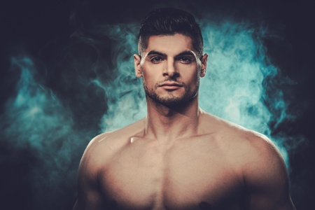 Handsome hispanic man with naked torso posing on smoked dark background.の写真素材