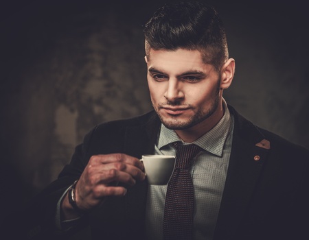 Serious well-dressed hispanic man with cup of coffee posing on dark background.の写真素材