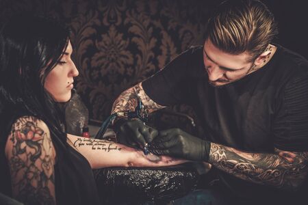 Professional tattoo artist makes a tattoo on a young girl's hand.の写真素材