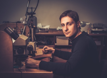 Jeweler sitting at his workplace in a workshop.の写真素材