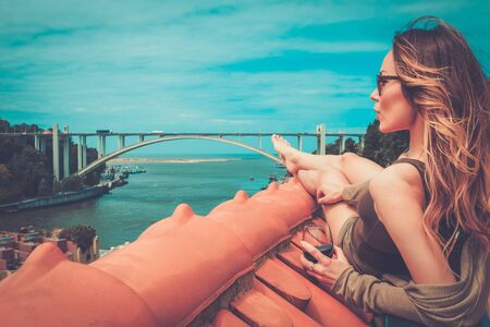 Woman enjoying sunbath with glass of port wine on the rooftop, on river bridge background.の写真素材