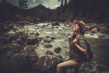 Beautiful woman hiker standing near wild mountain river.の写真素材