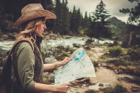 Woman hiker, searching right direction on map near wild mountain river.の写真素材