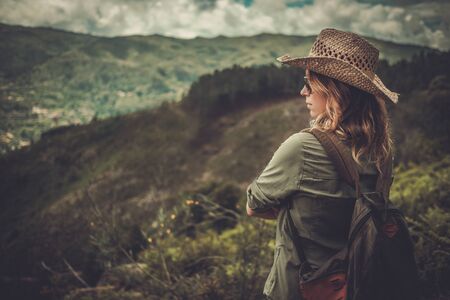 Woman hiker with backpack enjoying amazing valley landscapes on a top of mountain.