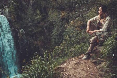 Beautiful woman hiker sitting near waterfall in deep forest.の写真素材