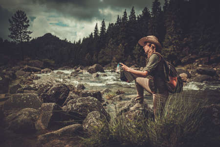Woman hiker, searching right direction on map near wild mountain river.の写真素材