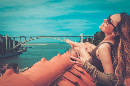 Woman enjoying sunbath with glass of port wine on the rooftop, on river bridge background.の写真素材