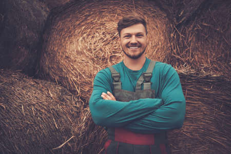 Confident young farmer standing near haystacks in his farm.の写真素材