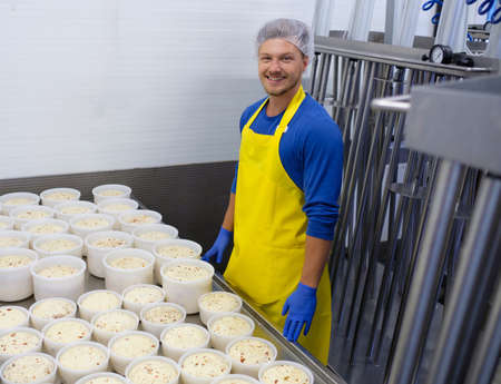 Handsome cheesemaker is checking cheeses in his workshop storage.
