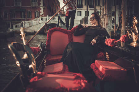 Beautiful woman in black dress with carnaval mask riding on gondola. の写真素材