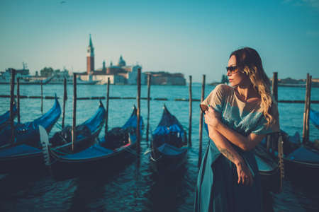 Beautiful well-dressed woman standing near San Marco square with gondolas and Saint George island on the background.の写真素材