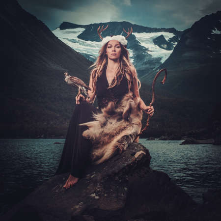 Nordic goddess in ritual garment with hawk near wild mountain lake in Innerdalen valley, Norway.の写真素材