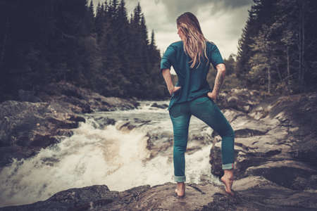 Confident woman posing near waterfall with mountain forest on the background.の写真素材