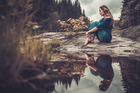 Confident woman posing near pond with mountain forest on the background.の写真素材