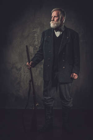Senior hunter with a shotgun in a traditional shooting clothing on a dark background.の写真素材
