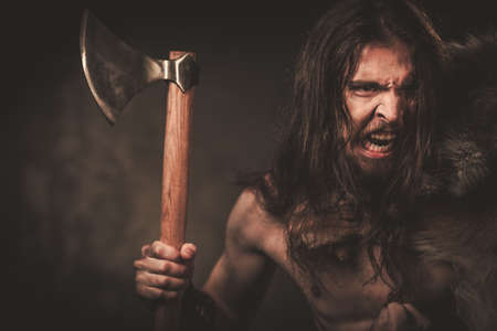 Viking with ax in a traditional warrior clothes, posing on a dark background.の写真素材