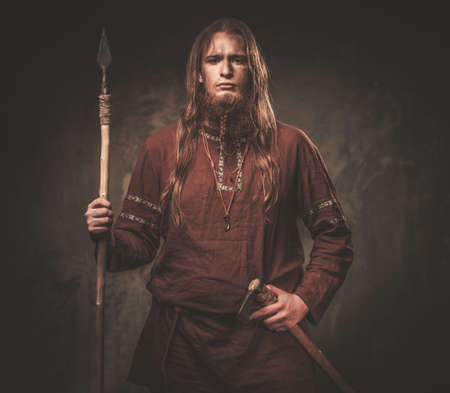 Serious viking with a spear in a traditional warrior clothes on a dark background.の写真素材