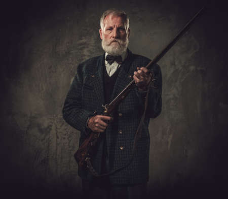 Senior hunter with a shotgun in a traditional shooting clothing on a dark background.の写真素材