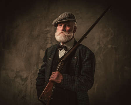 Senior hunter with a shotgun in a traditional shooting clothing on a dark background.の写真素材