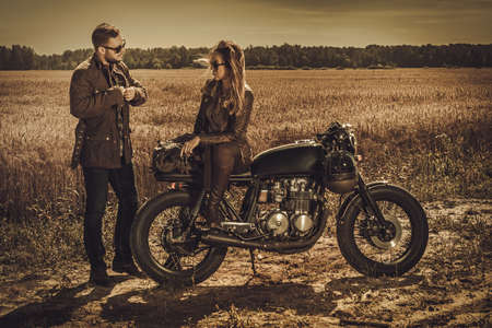 Young, stylish cafe racer couple on the vintage custom motorcycles in a field.の写真素材