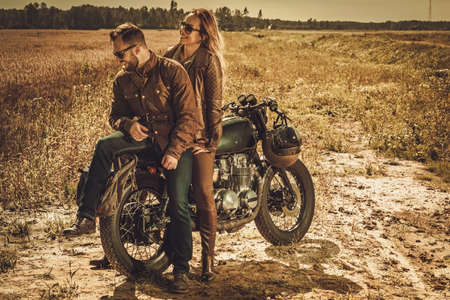 Young, stylish cafe racer couple on the vintage custom motorcycles in a field.の写真素材