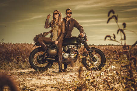 Young, stylish cafe racer couple on the vintage custom motorcycles in a field.の写真素材