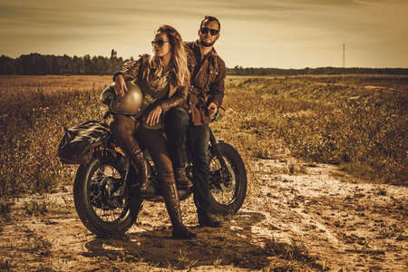 Young, stylish cafe racer couple on the vintage custom motorcycles in a field.の写真素材