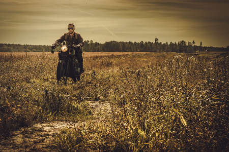 Young, stylish man on the vintage custom cafe racer in a field.の写真素材
