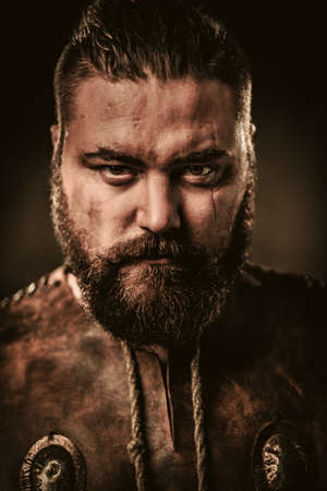 Serious viking in a traditional warrior clothes, posing on a dark background.の写真素材