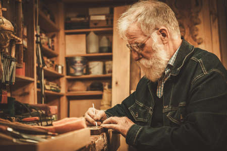 Senior restorer working with antique decor element in his workshop.