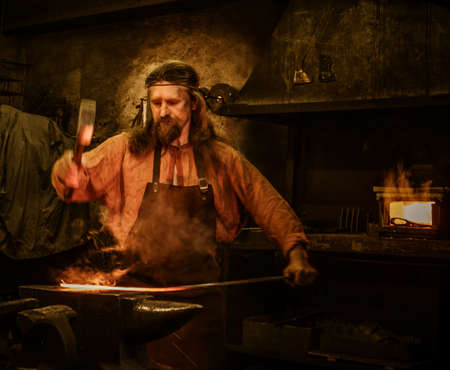 Senior blacksmith forging the molten metal on the anvil in smithy.の写真素材