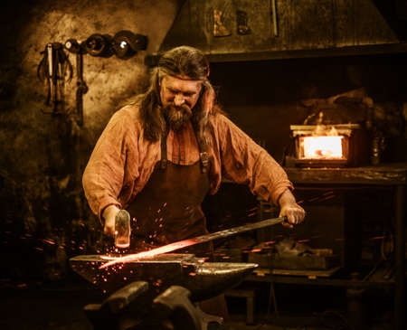 Senior blacksmith forging the molten metal on the anvil in smithy.の写真素材