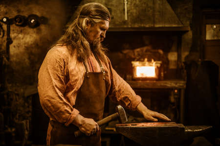 Senior blacksmith forging the molten metal on the anvil in smithy.の写真素材