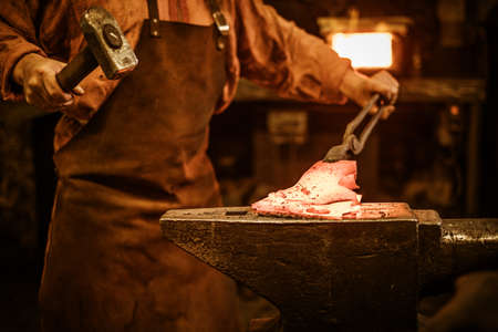 Senior blacksmith forging the molten metal on the anvil in smithy.の写真素材