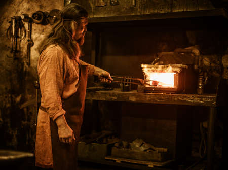 Senior blacksmith heats item before forgingin smithy.