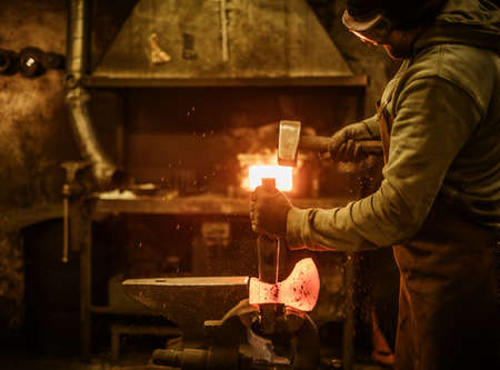The blacksmith forging the molten metal on the rusty vise in smithy.の写真素材
