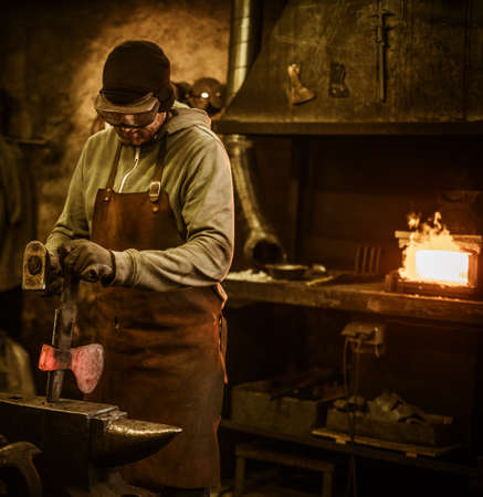 The blacksmith forging the molten metal on the anvil in smithy.