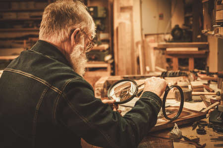 Senior restorer working with antique decor element in his workshop.