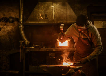 Blacksmith with brush handles the molten metal on the anvil in smithy.の写真素材