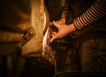 The blacksmith sharpening an ax on electrical grinder.