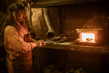 Senior blacksmith heats item before forgingin smithy.の写真素材