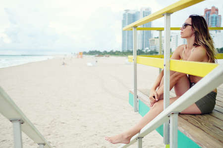 Beautiful woman in bikini sitting at the lifeguard station, Miami, USA