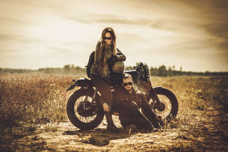 Stylish cafe racer couple on the vintage custom motorcycles in a field.の写真素材