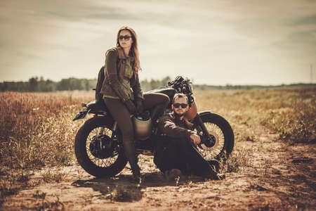Stylish cafe racer couple on the vintage custom motorcycles in a field.の写真素材