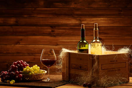 Bottles of red and white wine, glass and grape on a wooden interior.