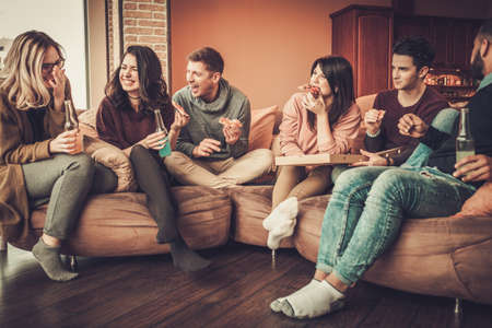 Group of multi ethnic young friends eating pizza in home interiorの写真素材