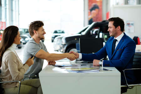 Salesman and customer shaking hands congratulating each other at the dealership showroom.の写真素材